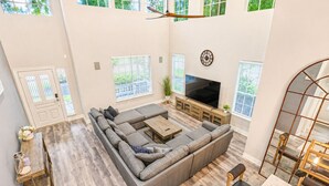 A spacious living room with a sectional sofa, a flat-screen TV, and a dining area with a table and chairs. - The Woodlands Gem- Heated Pool+Spa, EV Charging, Baby Crib, Ping Pong, Grill (The Woodlands)
