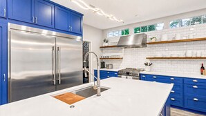 A modern kitchen with blue cabinets, stainless steel appliances, and a large island. - The Woodlands Gem- Heated Pool+Spa, EV Charging, Baby Crib, Ping Pong, Grill (The Woodlands)