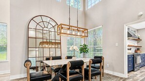 A dining area with a table, chairs, a hanging light fixture, and a large mirror. - The Woodlands Gem- Heated Pool+Spa, EV Charging, Baby Crib, Ping Pong, Grill (The Woodlands)