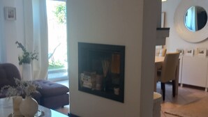 Una sala de estar moderna con chimenea, un comedor y una cocina visible al fondo.