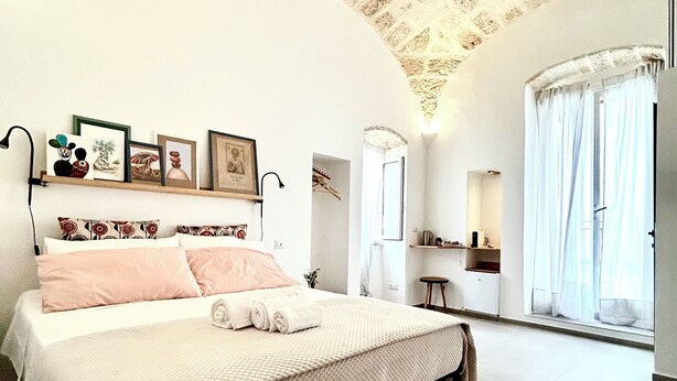A bedroom with a bed, a dresser, a mirror, and a window with curtains. - MIRA - Casa di Mare is a bright retreat in the heart of Polignano a Mare. (Polignano a Mare)