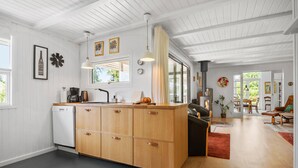 Eine moderne Küche mit Holdekor, einer Kaffeemaschine und einem Fenster. Durch eine offene Tür ist ein Essbereich mit Tisch und Stühlen zu sehen.