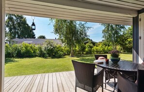 A covered outdoor patio with a table and chairs, overlooking a well-maintained lawn and garden. - 3 bedroom nice home in Odder (Odder)