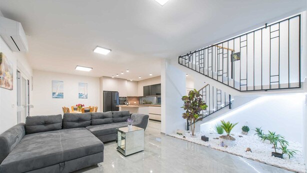 Una sala de estar moderna con un sofá seccional gris, una mesa de centro de vidrio y una escalera con barandilla de vidrio que conduce a un nivel superior.