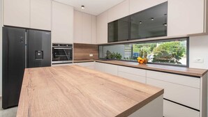 Una cocina moderna con encimera de madera, electrodomésticos integrados y un amplio ventanal con vistas a un jardín.