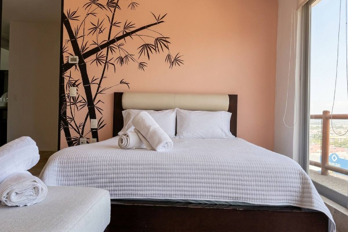 A hotel room with a bed, a sofa, a large window, and a bamboo wall decoration.