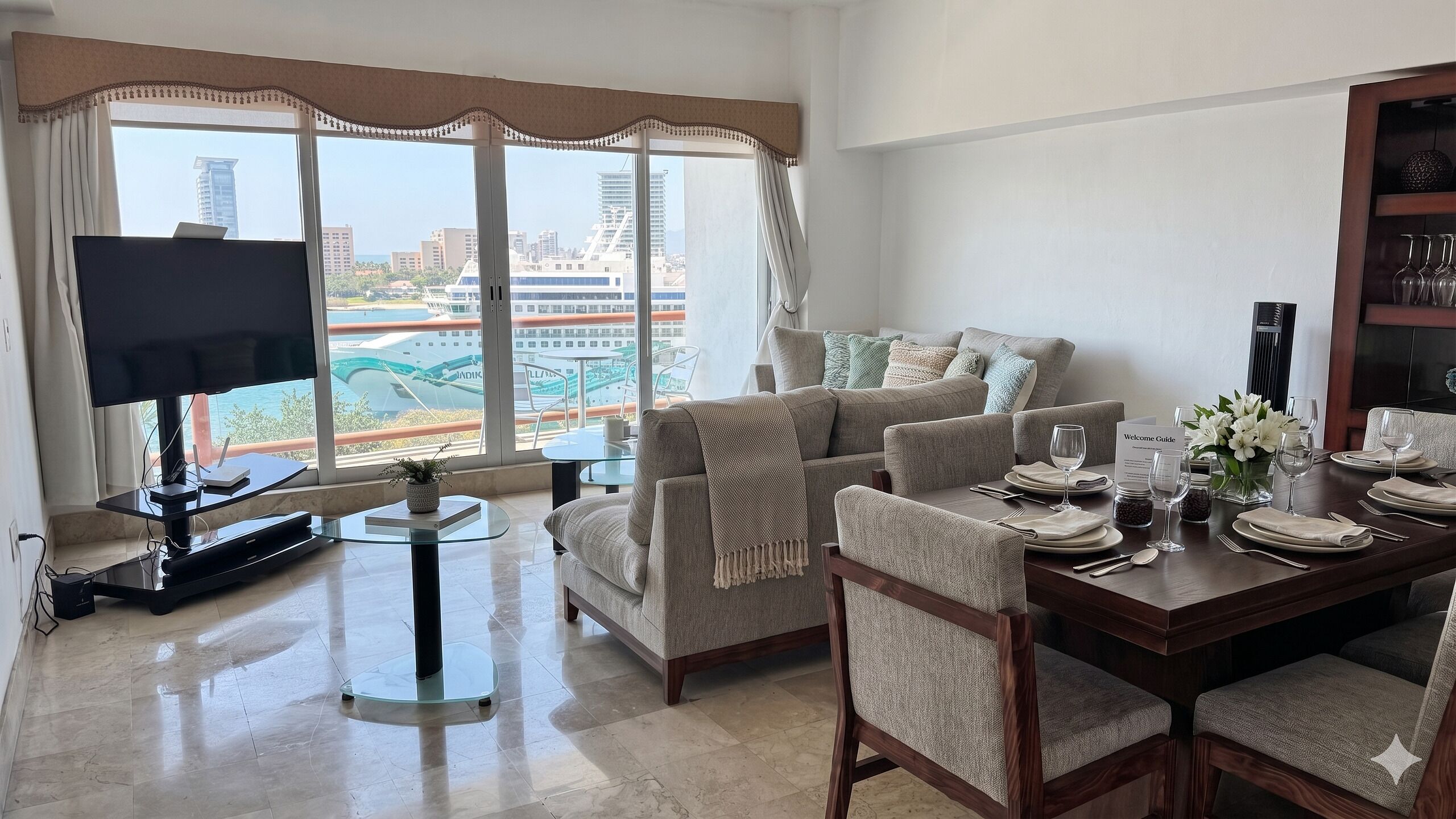 A modern living room with a TV, seating, dining area, and a view of a marina.