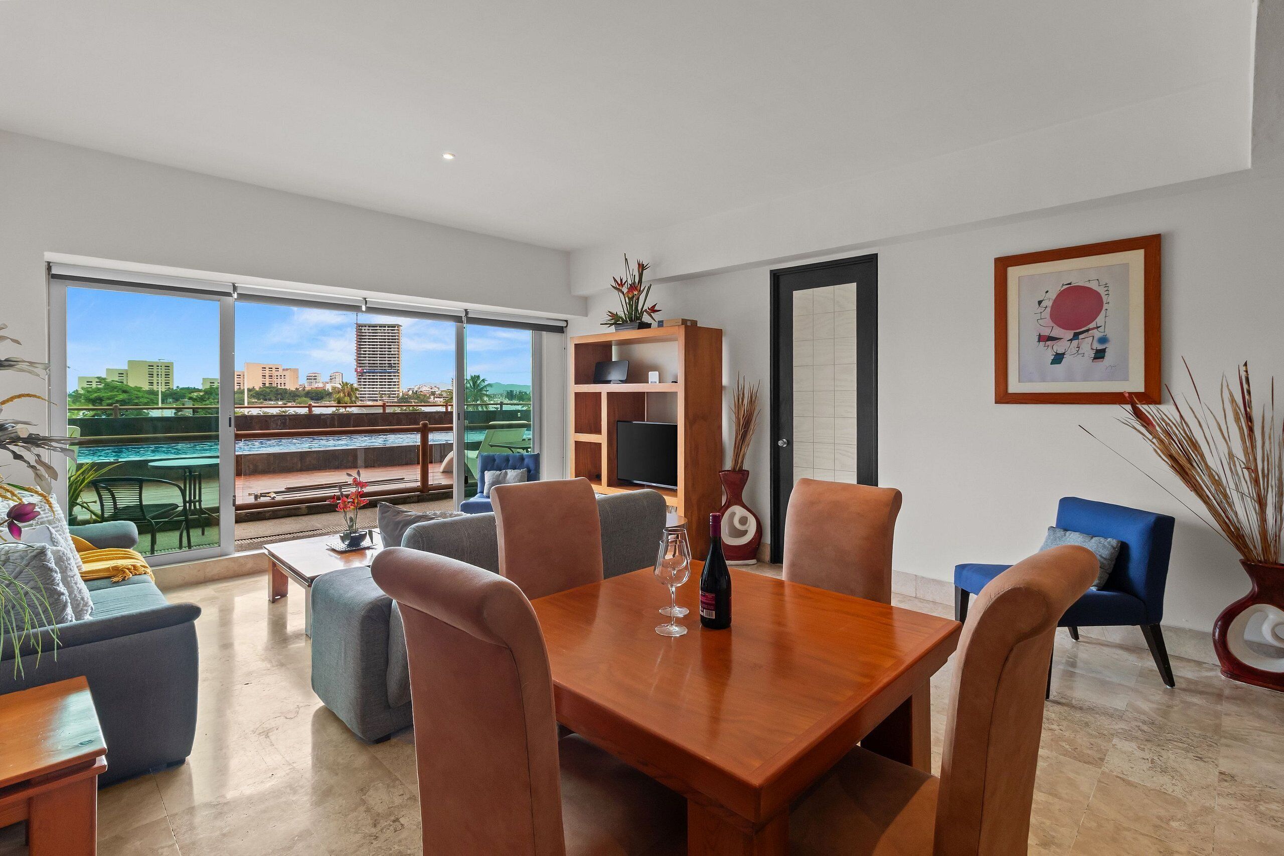 A modern living room with a dining area, large windows, and a view of a cityscape.