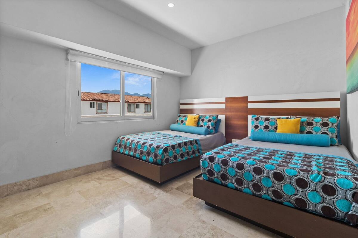 A bedroom with two beds, a window, and a view of buildings.