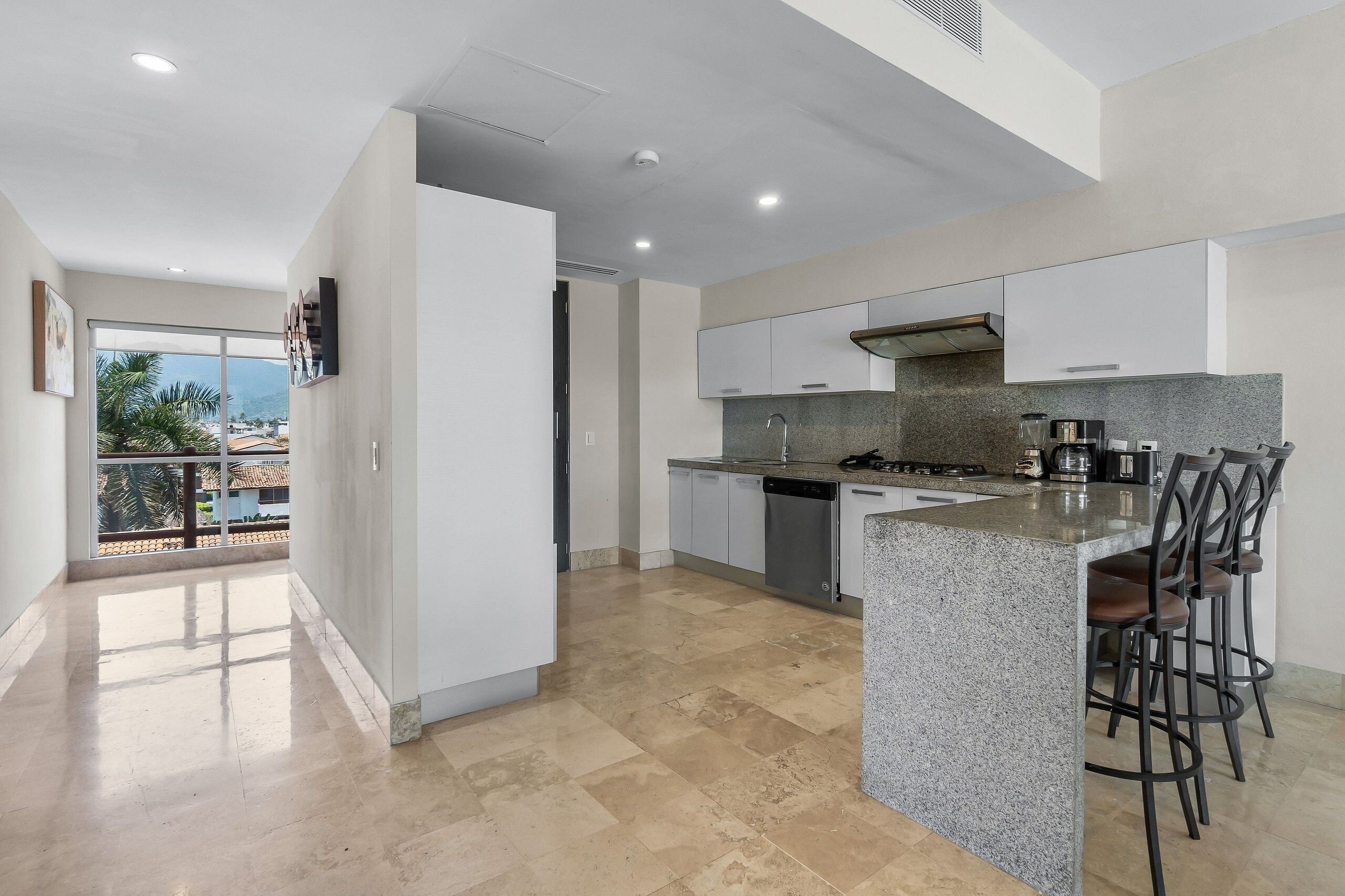 A modern kitchen with a central island, white cabinets, and a view to the outside.