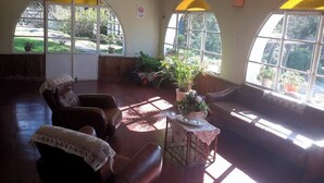 Habitación luminosa con grandes ventanales, un sofá, dos sillones y una mesita con una planta.