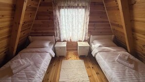 A cozy attic bedroom with two single beds, a small table, and a window with curtains. - Old Story Chalets (Žabljak)