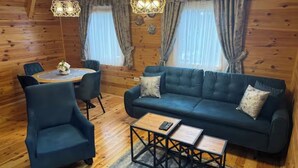 A cozy room with a dark blue sofa, a matching armchair, and a small wooden coffee table. There is a round table with chairs and a chandelier hanging from the ceiling. - Old Story Chalets (Žabljak)