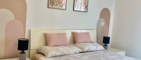 A bedroom with a bed, two nightstands, a dresser, and two wall-mounted lamps.