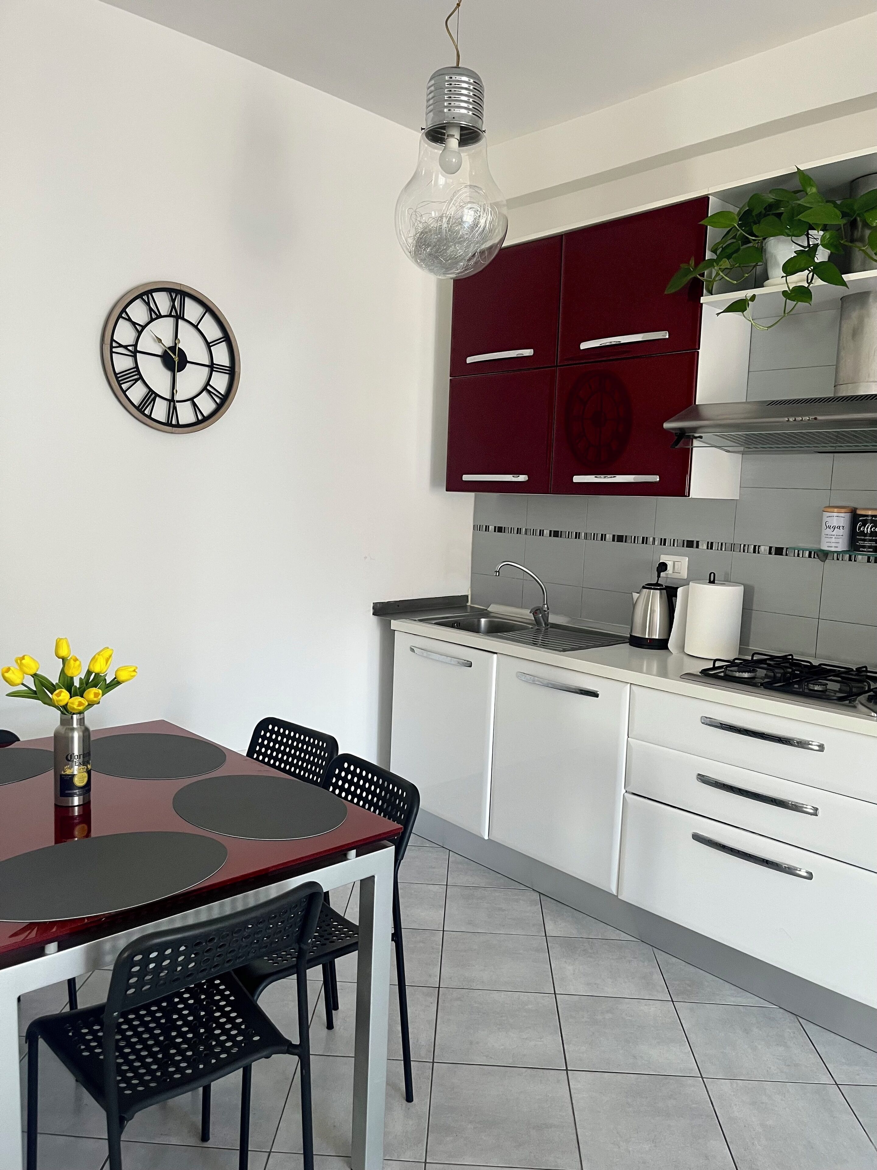 Una cucina moderna con mobili bianchi, una parete di accento rossa, un piano cottura in acciaio inossidabile e una zona pranzo con tavolo e sedie.