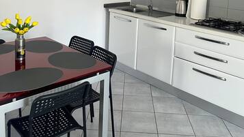 Una cucina moderna con mobili bianchi, una parete di accento rossa, un piano cottura in acciaio inossidabile e una zona pranzo con tavolo e sedie.