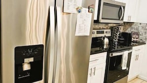 Une cuisine équipée d’appareils électroménagers en acier inoxydable, de meubles blancs, d’un four à micro-ondes et d’une bouilloire.