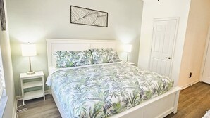 Une chambre à coucher comprenant un lit, des tables de chevet, une œuvre d’art murale et une porte.