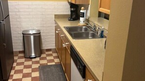 A compact kitchen with a checkered floor, a sink, a coffee maker, and a trash bin.