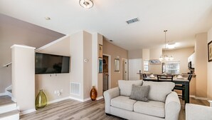 Un salon moderne avec un canapé, un coin repas comprenant une table et des chaises, et une cuisine en arrière-plan.