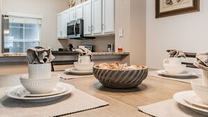 Une cuisine moderne avec des meubles blancs, un four à micro-ondes et un coin repas agrémenté d’assiettes et de bols blancs.