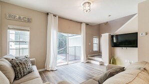 Un salon avec un canapé beige, un téléviseur à écran plat et un panneau indiquant « PLAGE ».