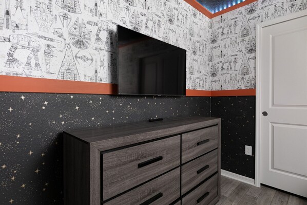 Una habitación con un muro lleno de estrellas, un televisor de pantalla plana y un aparador de madera.