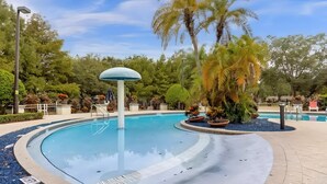 A swimming pool with a central fountain, surrounded by palm trees and a paved walkway.