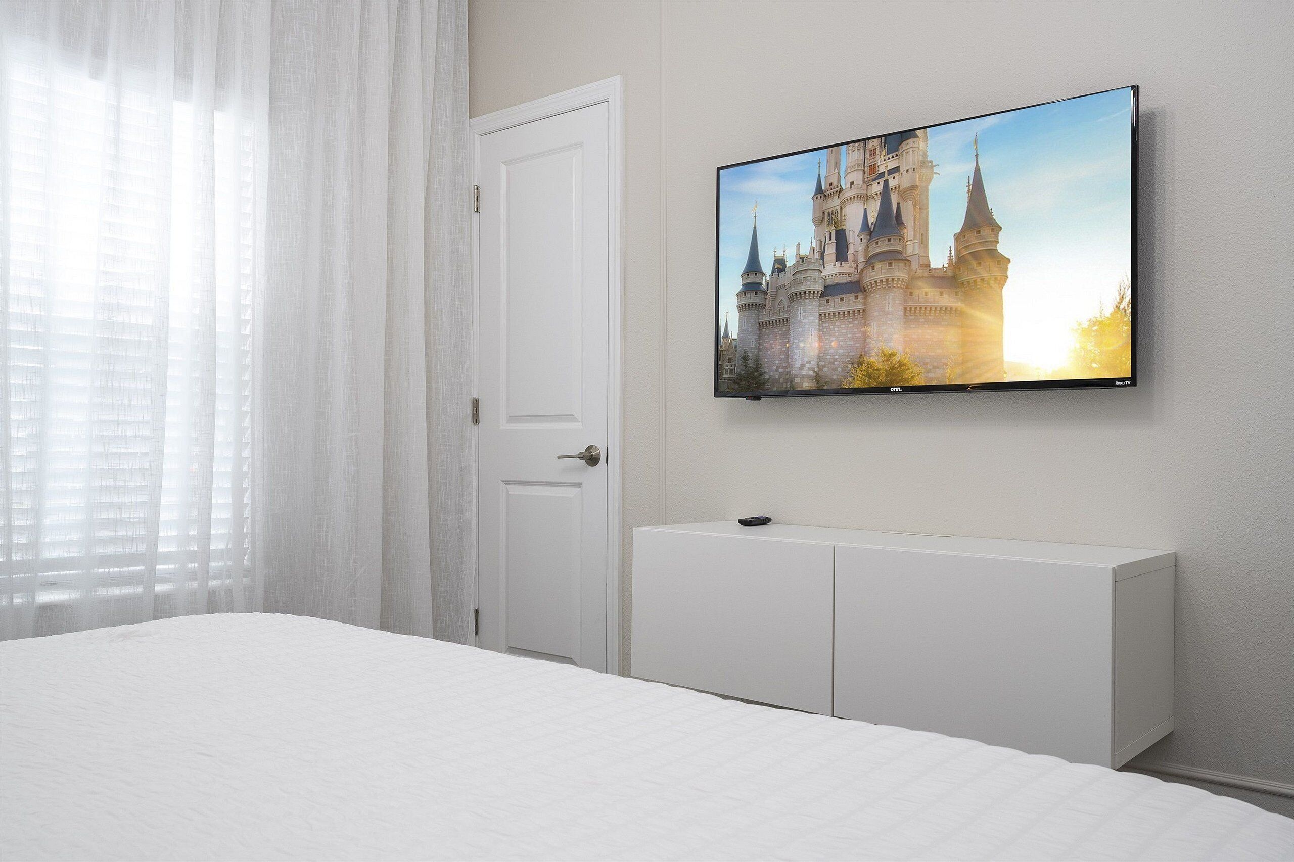 Habitación de hotel con una cama grande, un televisor en la pared mostrando un castillo y una puerta blanca.