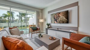 Una sala de estar moderna con un televisor de pantalla plana grande montado en la pared, un sofá con cojines, una mesa de centro y una silla.