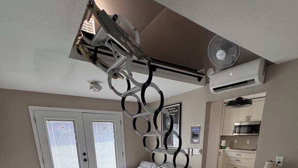 Un dormitorio moderno con cama, ventana grande, área de cocina y ventilador de techo.