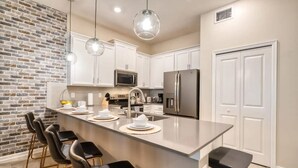 A modern kitchen with a brick accent wall, white cabinetry, stainless steel appliances, and a bar area with stools.