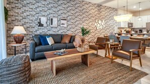 A modern living room with a brick wall, a sofa, a coffee table, and a dining area with chairs and a kitchen in the background.