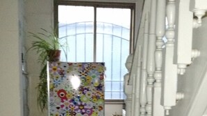 En hall med ett kylskåp täckt av färgglada blommönster, en krukväxt och en trappa med vita räcken.