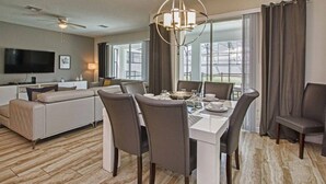 A modern living room with a dining area, a flat-screen TV, and a large window with curtains. - 6BR Home | Private Pool | 10 Min to Disney! (Kissimmee)