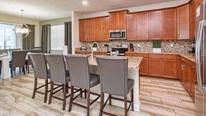A modern kitchen with wooden cabinets, a stainless steel refrigerator, and a granite countertop. - 6BR Home | Private Pool | 10 Min to Disney! (Kissimmee)