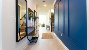 Un pasillo con pared azul, una consola de madera con jarrones y una escalera al fondo.