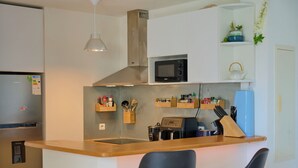 A modern kitchen with a built-in microwave, a water dispenser, and wooden shelves with kitchen utensils and spices. - L'horizon bleu : Sea view, air-conditioning, swimming pool, near airport and hospital for 4 people (Saint-Denis)