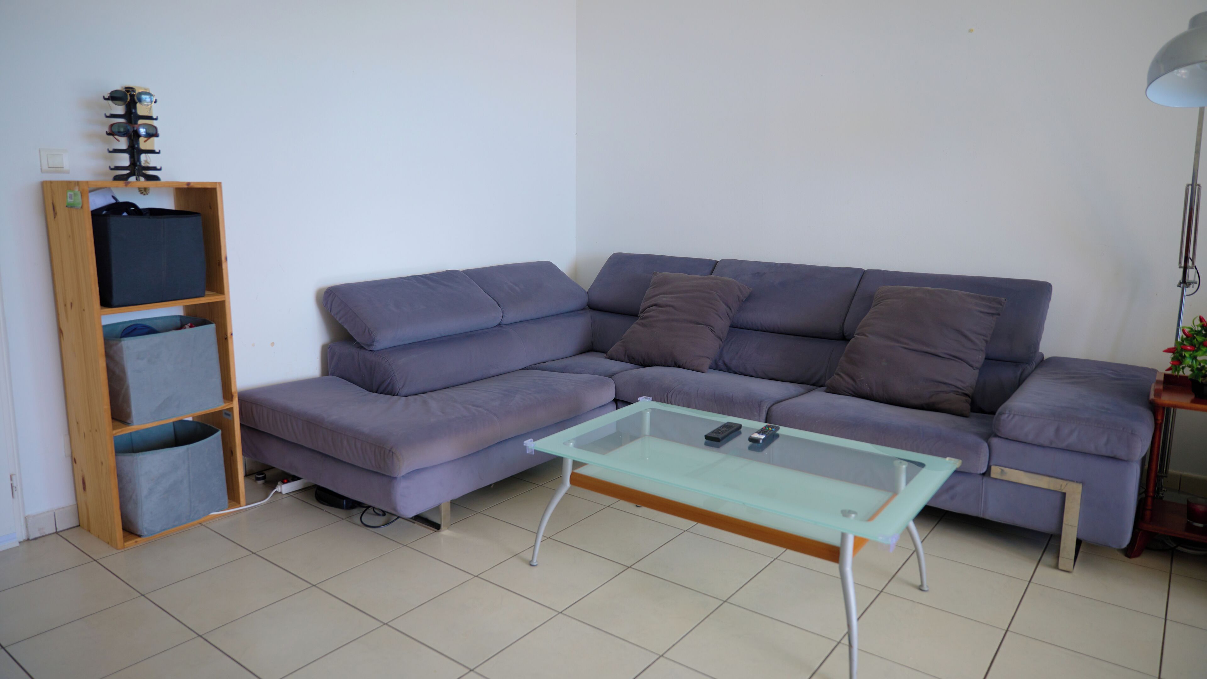 Een woonkamer met een grijze modulaire bank, een glazen salontafel en een houten wandrek met opbergmanden.