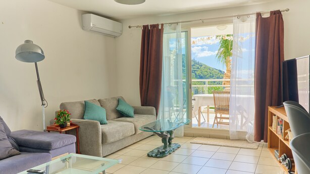 A living room with a sofa, a glass coffee table, a lamp, a TV, and a balcony with a table and chairs. - L'horizon bleu : Sea view, air-conditioning, swimming pool, near airport and hospital for 4 people (Saint-Denis)