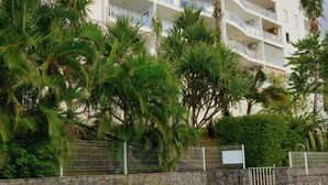A swimming pool with a stone border, surrounded by palm trees and a multi-story building with balconies. - L'horizon bleu : Sea view, air-conditioning, swimming pool, near airport and hospital for 4 people (Saint-Denis)