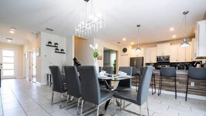 A modern kitchen with stainless steel appliances, a dining area with a glass table and black chairs, and a chandelier.