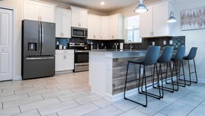 A modern kitchen with white cabinets, stainless steel appliances, a central island with bar stools, and pendant lighting.