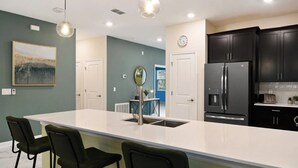 Une cuisine moderne dotée d’un grand îlot central, de meubles de couleur noire, d’appareils électroménagers en acier inoxydable et de luminaires suspendus.