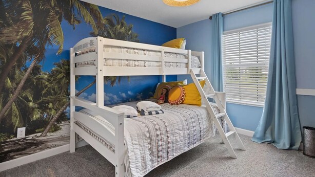 A bunk bed with a ladder, a wall mural of palm trees, a window with blinds, and a hanging light fixture.