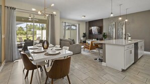 A modern kitchen with a central island, dining area with chairs and a table set for four, and a living area with a sofa and TV. - Themed Home w/ Private Pool (Davenport)