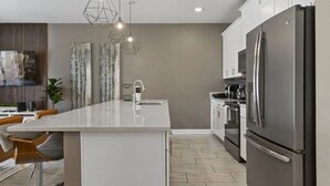A modern kitchen with a central island, stainless steel appliances, pendant lighting, and a dining area with bar stools. - Themed Home w/ Private Pool (Davenport)