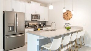 Une cuisine moderne dotée d’appareils électroménagers en acier inoxydable, d’un îlot central avec des tabourets de bar et d’un éclairage suspendu.