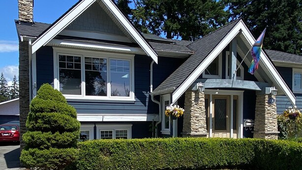 A two-story house with a stone facade, a well-maintained lawn, and a flag. - Raven’s Nest – Cozy Lower One‑Bedroom Suite (Victoria)