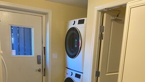 A laundry room with two stacked front-loading washers and dryers, a trash can, and a black mat leading to a door. - Raven’s Nest – Cozy Lower One‑Bedroom Suite (Victoria)